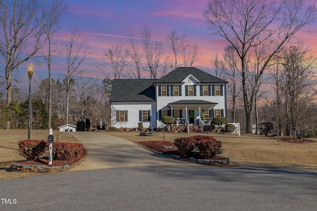 colonial-style house featuring driveway, covered porch, and roof with shingles