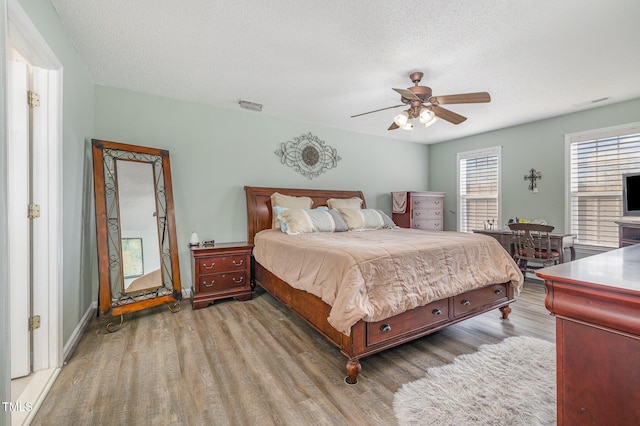 bedroom with a ceiling fan, visible vents, a textured ceiling, and wood finished floors