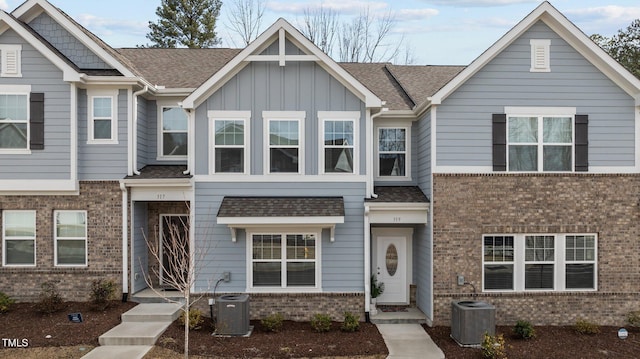 multi unit property featuring roof with shingles, brick siding, board and batten siding, and central air condition unit