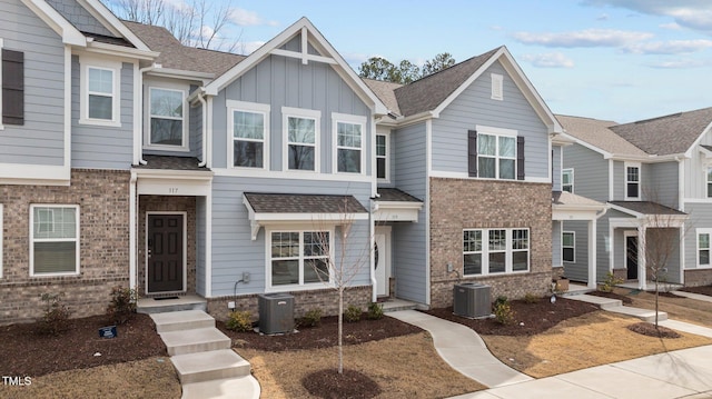 townhome / multi-family property with brick siding, board and batten siding, a shingled roof, and cooling unit