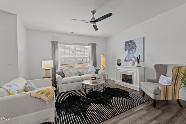 living room with ceiling fan, a fireplace, baseboards, and wood finished floors