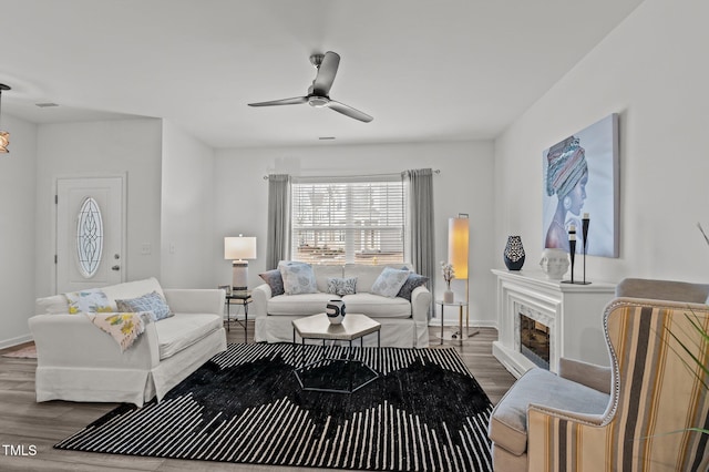 living area featuring visible vents, a glass covered fireplace, ceiling fan, wood finished floors, and baseboards