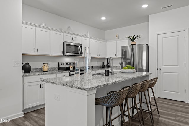 kitchen with an island with sink, dark wood-style floors, stainless steel appliances, a kitchen bar, and white cabinetry