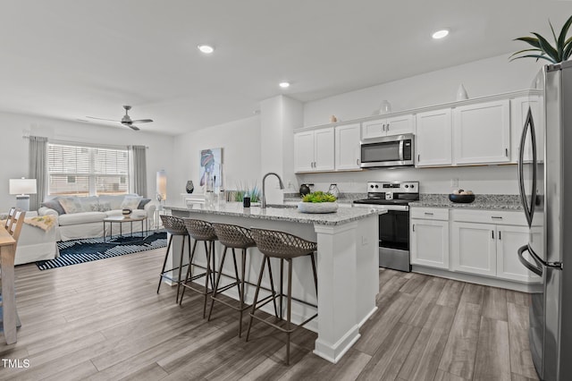 kitchen featuring white cabinets, light wood-style flooring, a breakfast bar area, open floor plan, and stainless steel appliances