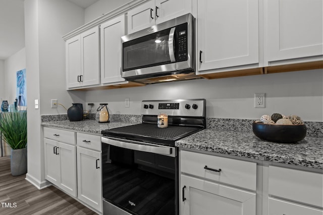 kitchen with stainless steel appliances, white cabinets, light wood-style flooring, and light stone countertops