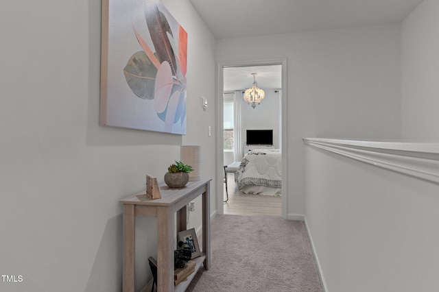 corridor featuring carpet, baseboards, and a chandelier