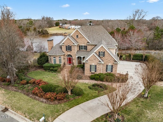 traditional-style house featuring a shingled roof, a chimney, a water view, a front lawn, and brick siding