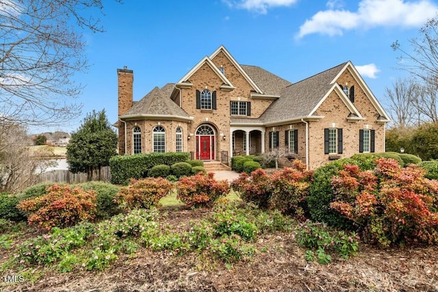 view of front of house with brick siding, a chimney, a shingled roof, and fence