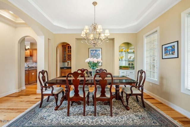 dining room with crown molding, a notable chandelier, a raised ceiling, light wood-style floors, and baseboards