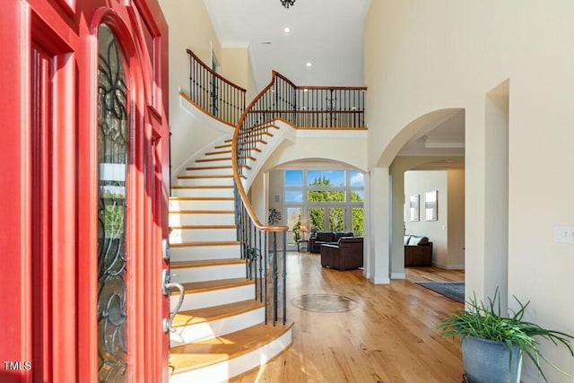 foyer featuring arched walkways, wood finished floors, a towering ceiling, stairs, and ornamental molding