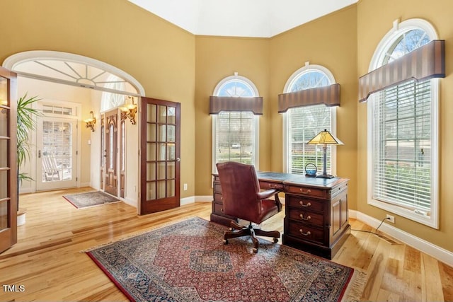 office space featuring light wood-type flooring, a towering ceiling, and baseboards