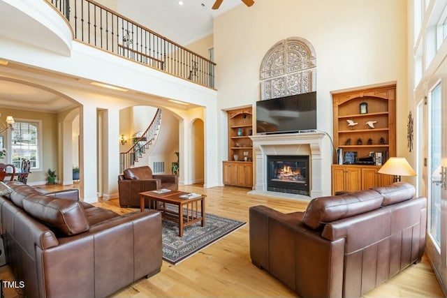 living room with arched walkways, crown molding, a glass covered fireplace, light wood-type flooring, and stairs