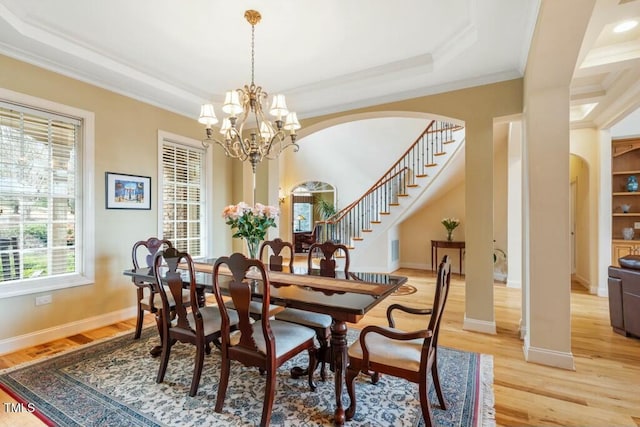 dining room with light wood-style floors, a notable chandelier, arched walkways, and crown molding