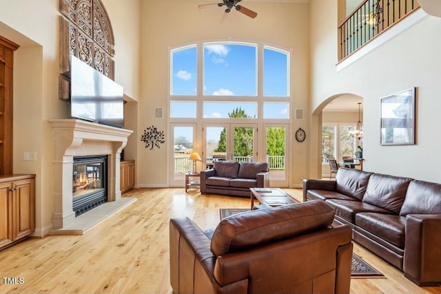 living room featuring arched walkways, a high ceiling, light wood-style floors, a glass covered fireplace, and baseboards