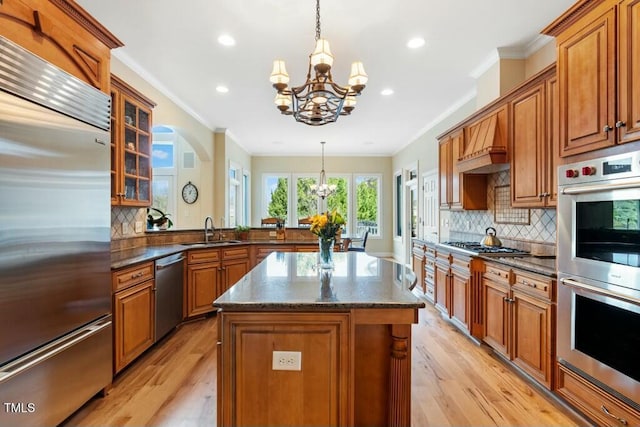 kitchen with a chandelier, a peninsula, a sink, appliances with stainless steel finishes, and brown cabinetry