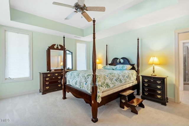 bedroom featuring ceiling fan, a tray ceiling, baseboards, and light colored carpet