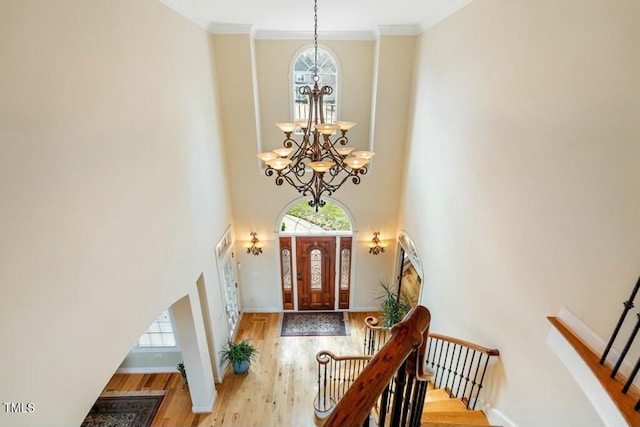 entrance foyer with crown molding, a notable chandelier, stairway, wood finished floors, and baseboards