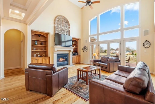 living room with arched walkways, crown molding, light wood finished floors, a fireplace with flush hearth, and baseboards