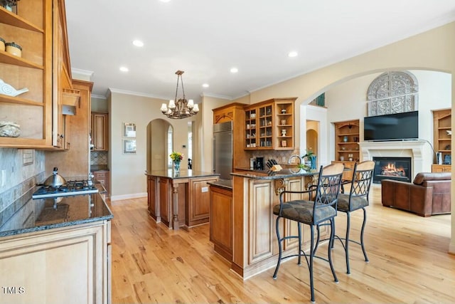 kitchen with brown cabinetry, a glass covered fireplace, stainless steel appliances, a kitchen bar, and open shelves