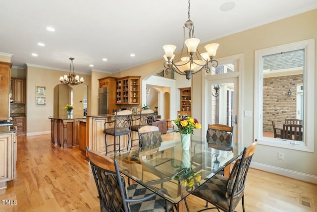 dining area with arched walkways, light wood finished floors, and a notable chandelier