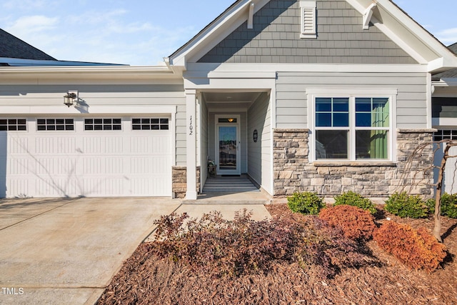 doorway to property with stone siding, an attached garage, and concrete driveway