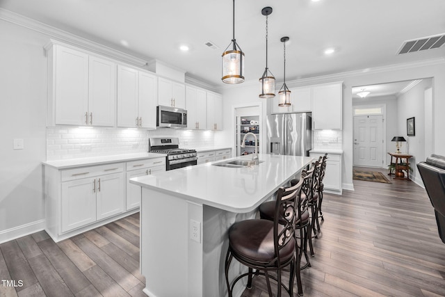 kitchen with stainless steel appliances, visible vents, ornamental molding, a sink, and wood finished floors