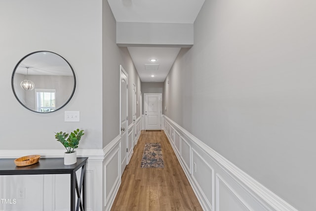 hall with light wood-style floors, a decorative wall, and wainscoting