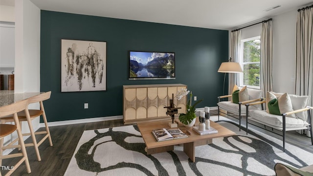 living area featuring an accent wall, dark wood-style flooring, visible vents, and baseboards