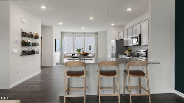 kitchen featuring visible vents, dark wood finished floors, appliances with stainless steel finishes, tasteful backsplash, and a kitchen bar