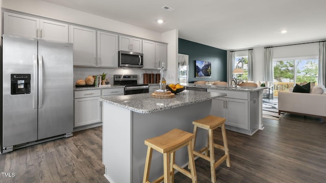 kitchen featuring a kitchen island, a kitchen breakfast bar, dark wood-type flooring, stainless steel appliances, and gray cabinetry