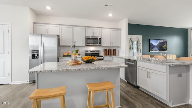 kitchen with dark wood finished floors, stainless steel appliances, visible vents, a peninsula, and a kitchen bar