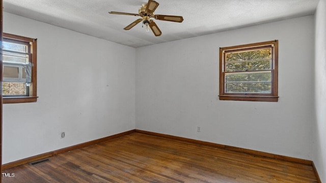 spare room featuring dark wood-style floors, a wealth of natural light, visible vents, and baseboards