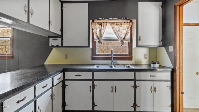 kitchen with dark countertops, a sink, and white cabinetry