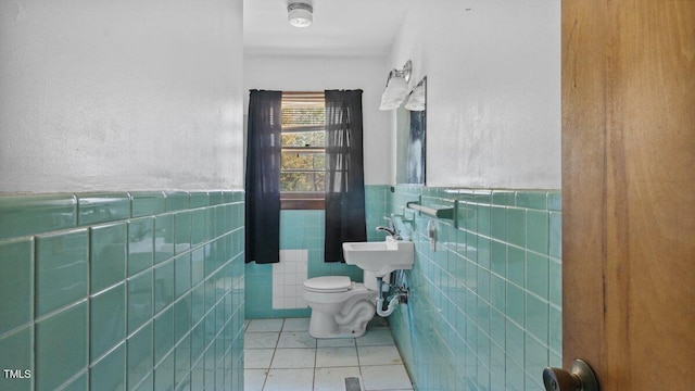 half bath with wainscoting, tile patterned flooring, toilet, and tile walls