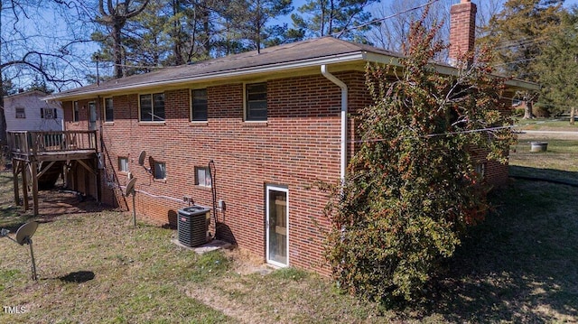 view of side of property with a chimney, central AC unit, a lawn, and brick siding