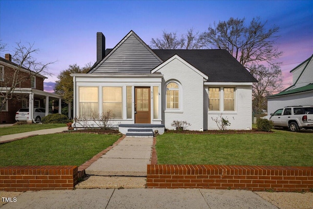 bungalow-style home with a front yard, brick siding, and a chimney