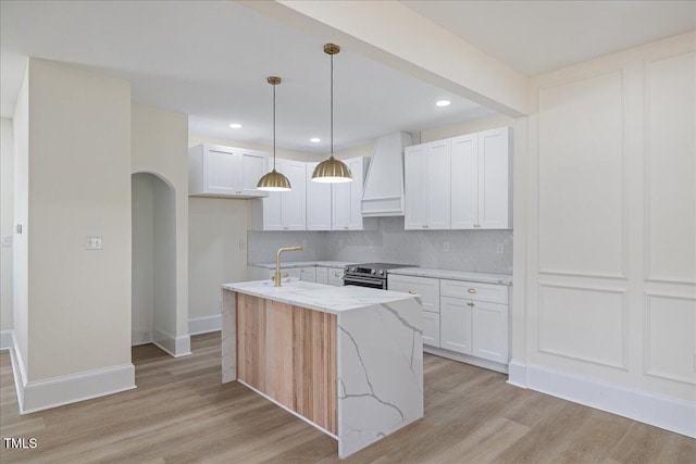 kitchen featuring arched walkways, stainless steel electric range oven, light wood-style flooring, light stone counters, and custom exhaust hood