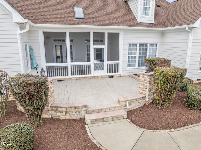 view of exterior entry featuring a shingled roof and a patio