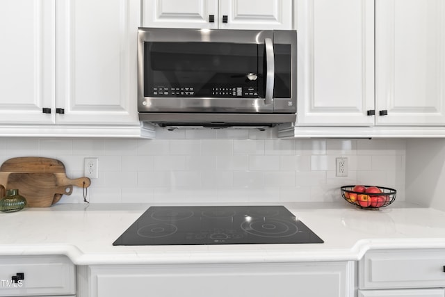 kitchen featuring decorative backsplash, stainless steel microwave, black electric stovetop, and white cabinetry