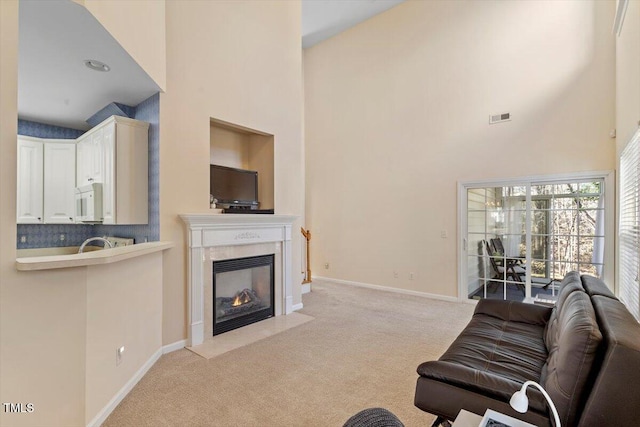 carpeted living room with a fireplace with flush hearth, baseboards, visible vents, and a high ceiling