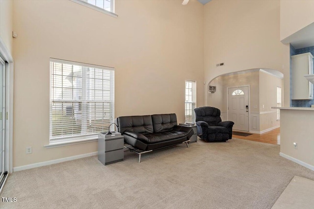 living area featuring light carpet, baseboards, visible vents, and arched walkways