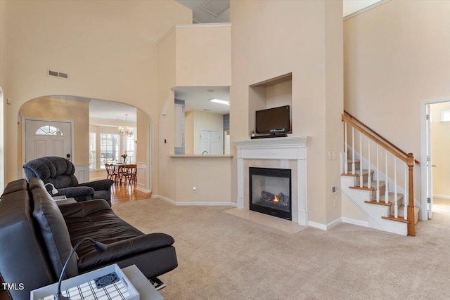 carpeted living room with arched walkways, a fireplace with flush hearth, a towering ceiling, visible vents, and stairway