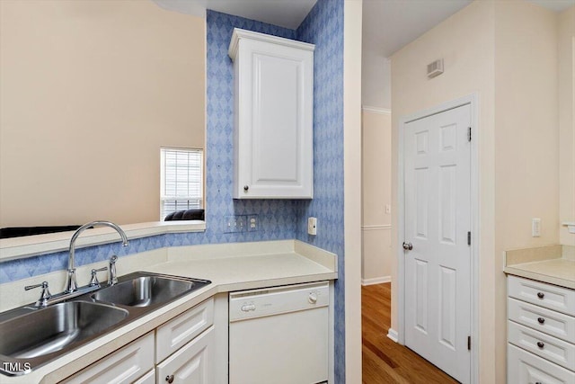 kitchen with wallpapered walls, white dishwasher, light countertops, white cabinetry, and a sink