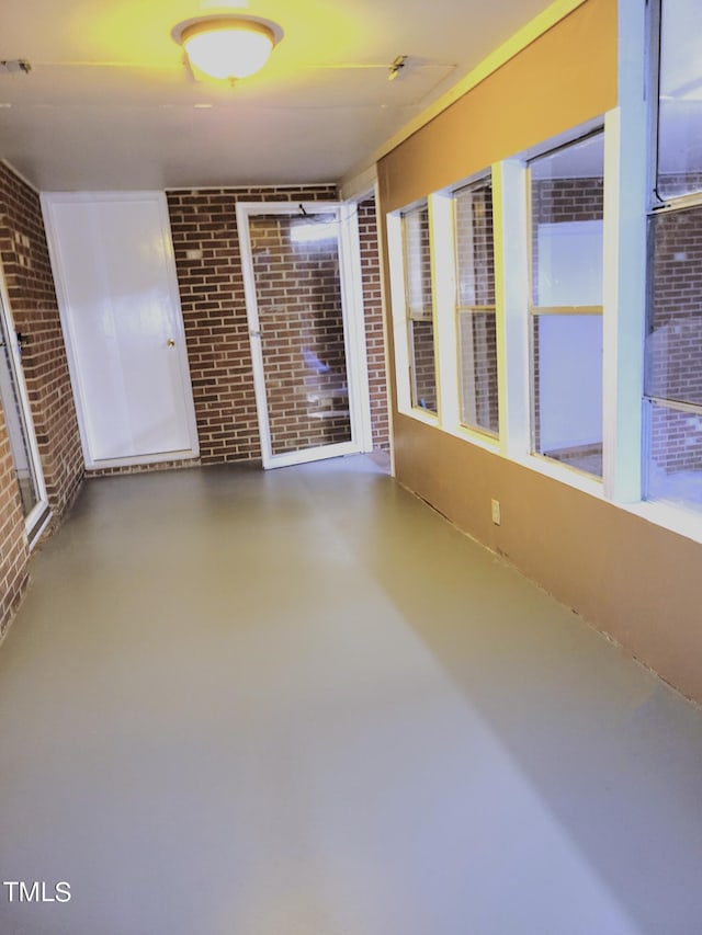 empty room featuring concrete flooring, a sunroom, and brick wall