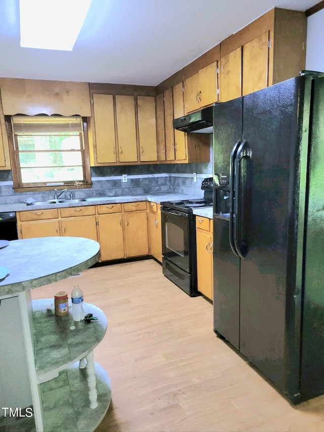 kitchen with tasteful backsplash, under cabinet range hood, light wood-type flooring, black appliances, and a sink