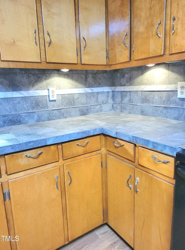 kitchen with brown cabinetry, light wood-type flooring, and backsplash