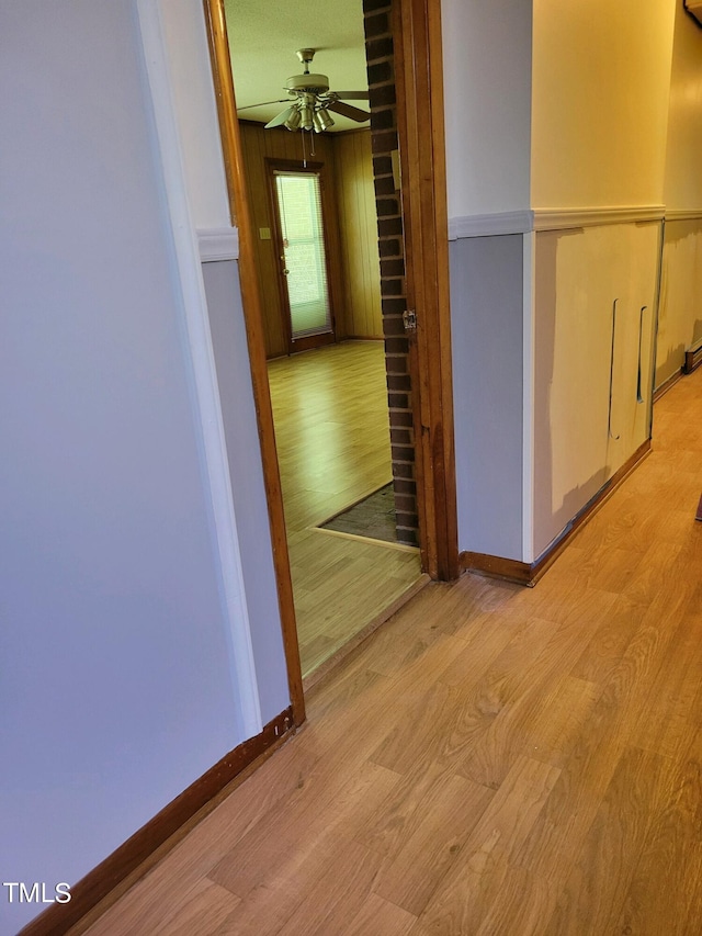 corridor with baseboards, light wood finished floors, and wooden walls