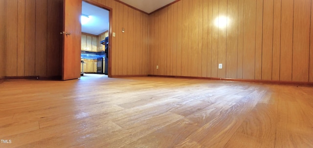 spare room with crown molding, wooden walls, baseboards, and wood finished floors