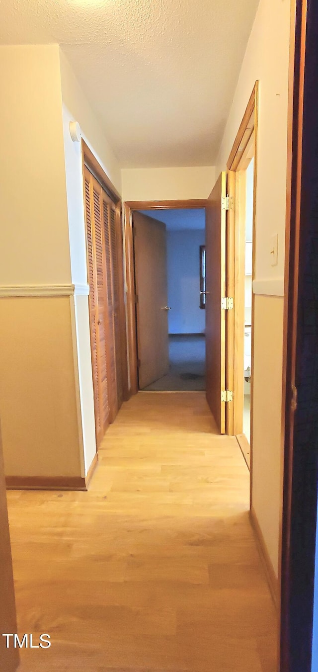 corridor with a textured ceiling, baseboards, and wood finished floors