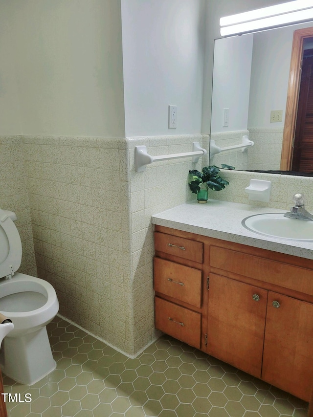 half bath featuring toilet, wainscoting, vanity, and tile walls